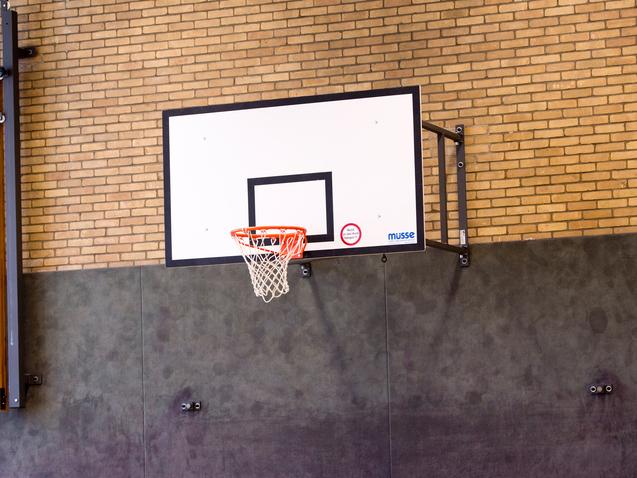 Basketballkorb an einer Wand mit Sprossenwand im Hintergrund in einer Sporthalle.
