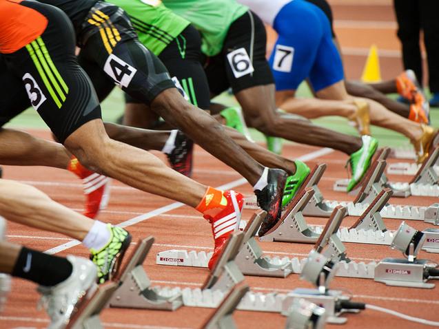 Start einer Sprintveranstaltung mit mehreren Athleten in Blockstartposition auf einer Laufbahn.