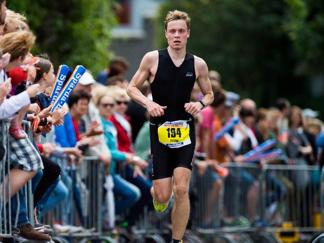 Ein Athlet sprintet entlang einer Zuschauerreihe bei einem Wettkampf, während die Menge jubelt und applaudiert.