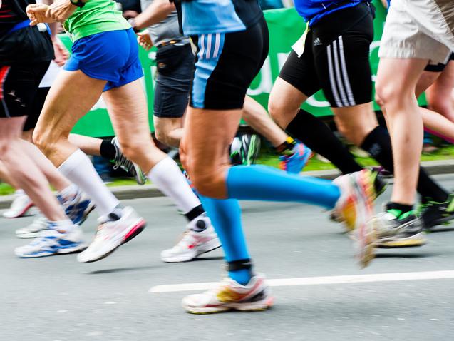 Bunte Laufschuhe rennen in einem Marathon, während Zuschauer im Hintergrund auf der Strecke stehen.