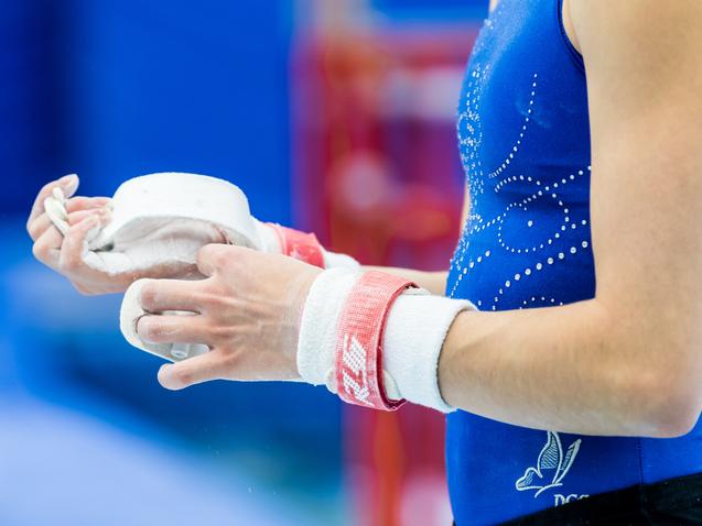 Nahaufnahme einer Sportlerin mit Kreide in der Hand, die ihre Hände mit einem roten Handgelenkschutz umwickelt.